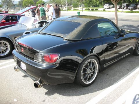 1998 Ford Crown Victoria - A black convertible sports car is parked next to other vehicles at an outdoor gathering.
