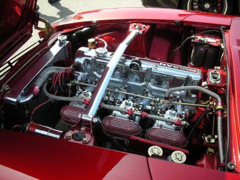 1998 Ford Crown Victoria - The engine bay of a red Nissan features a polished intake manifold and custom air filters.