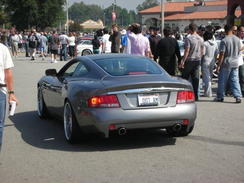 1998 Ford Crown Victoria - A gray Aston Martin Vanquish is seen from the rear at an outdoor gathering of vehicles and people.