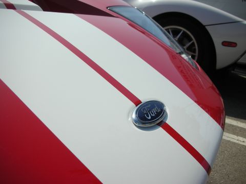 1998 Ford Crown Victoria - A close-up of a Ford emblem on a car with racing stripes, parked next to another vehicle.