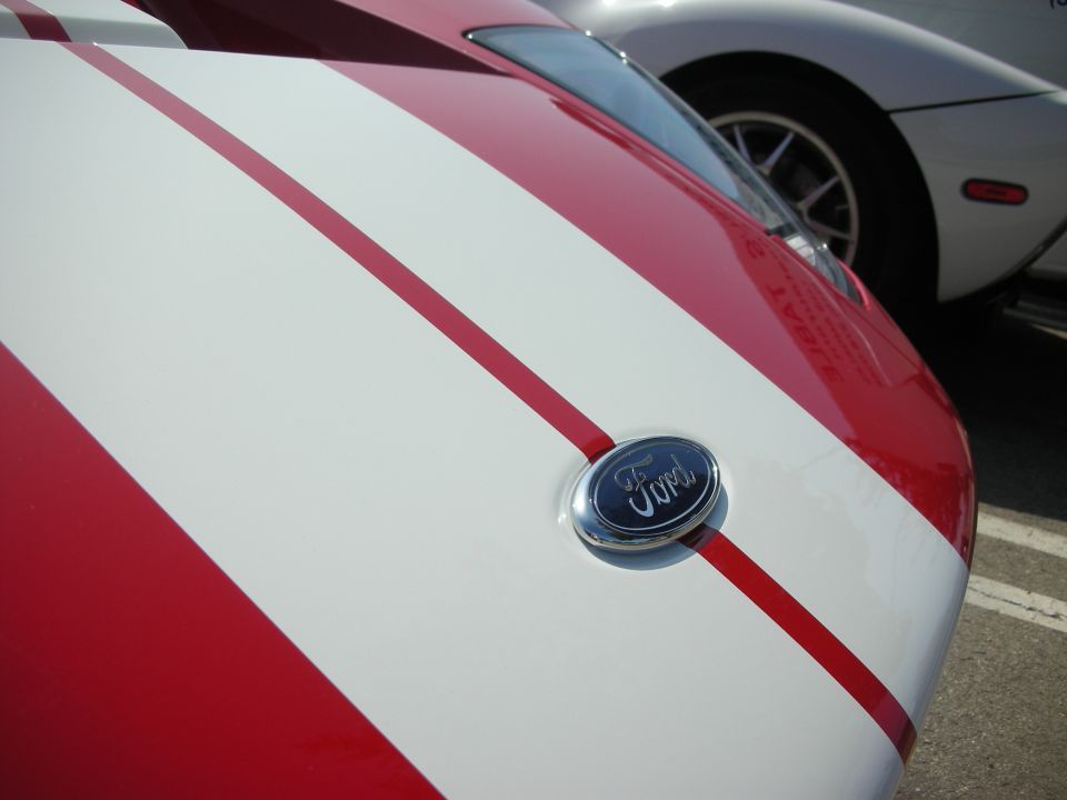 Ford emblem on a red and white striped car hood, with another white car visible behind it
