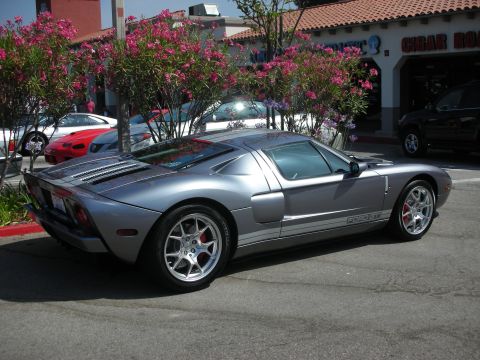 1998 Ford Crown Victoria - A silver Ford GT is parked in front of a building with flowering bushes and other vehicles.