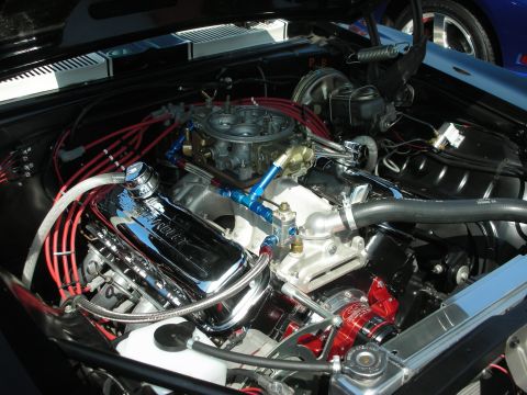 1998 Ford Crown Victoria - The engine bay of a car, chrome Chevrolet valve covers and a Holley carburetor, with another vehicle visible in the background.