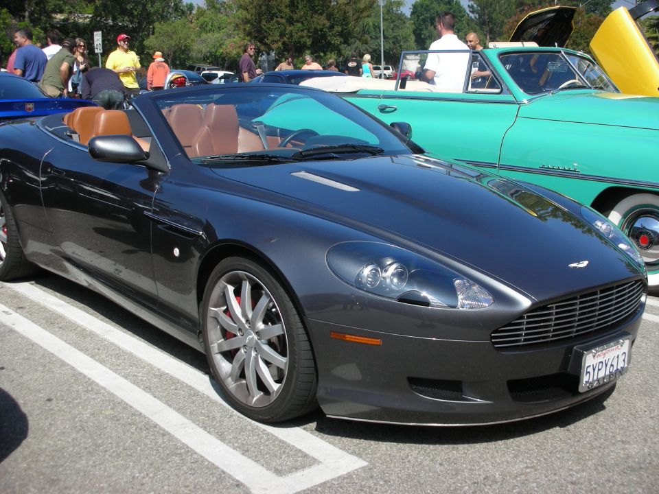 Dark gray Aston Martin DB9 Volante convertible parked next to a teal classic car
