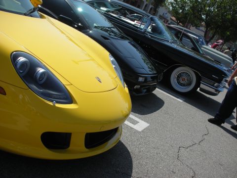 1998 Ford Crown Victoria - A line of cars, including a yellow sports car and a classic black car, are parked in a lot.