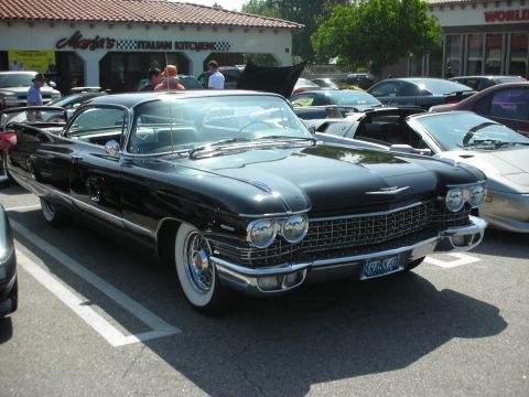 1998 Ford Crown Victoria - A classic black Cadillac convertible is parked in a lot with other vehicles and a building in the background.