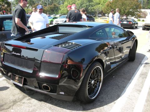 1998 Ford Crown Victoria - A black Lamborghini Gallardo is parked at an outdoor gathering with other vehicles and people around.