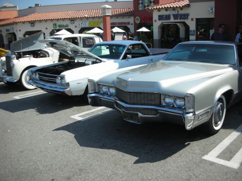 1998 Ford Crown Victoria - A silver Cadillac is parked in a lot with its front end facing the camera, showing off its distinctive grille and headlights.