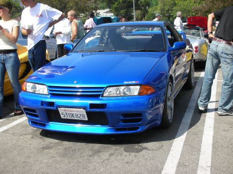 1998 Ford Crown Victoria - A bright blue Nissan Skyline GT-R R32 is parked at a car meet, with other vehicles and people around.