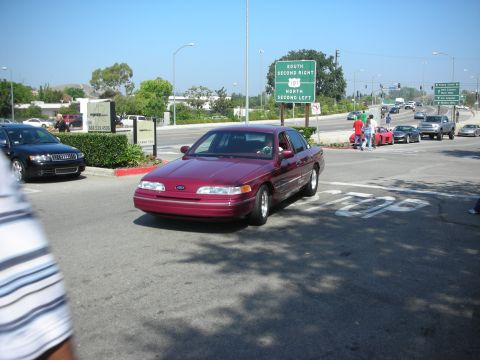 1998 Ford Crown Victoria - A maroon 1998 Ford Crown Victoria sedan is seen at an intersection with a highway sign in the background.