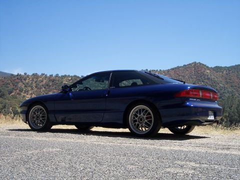 1995 Ford Probe - A blue 1995 Ford Probe is parked on a gravel surface with a hilly landscape under a clear blue sky.