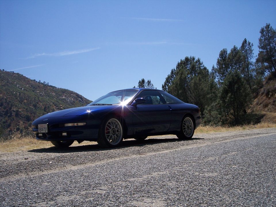 Blue 1995 Ford Probe with aftermarket wheels parked on a gravel road