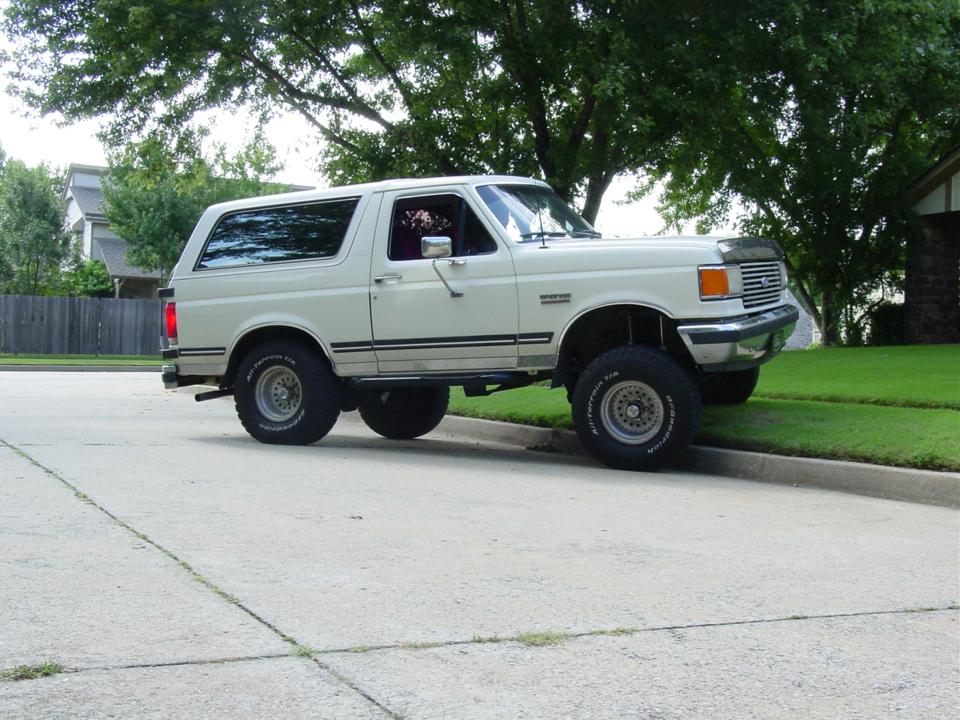 Lifted white two-door Ford Bronco on all-terrain tires, passenger side view in a driveway