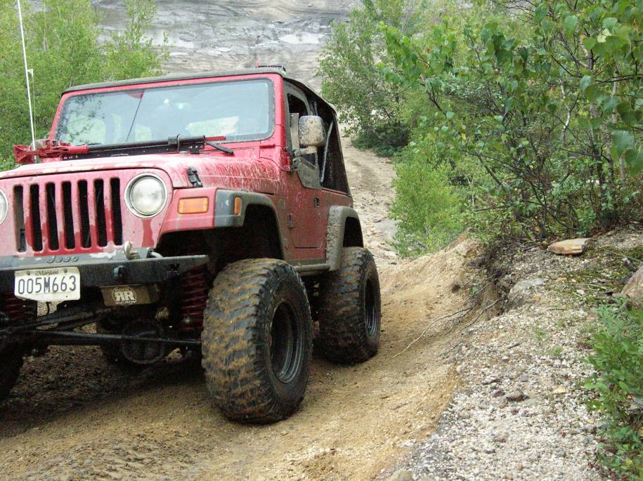 Red 2003 Jeep Wrangler with large tires on a dirt trail