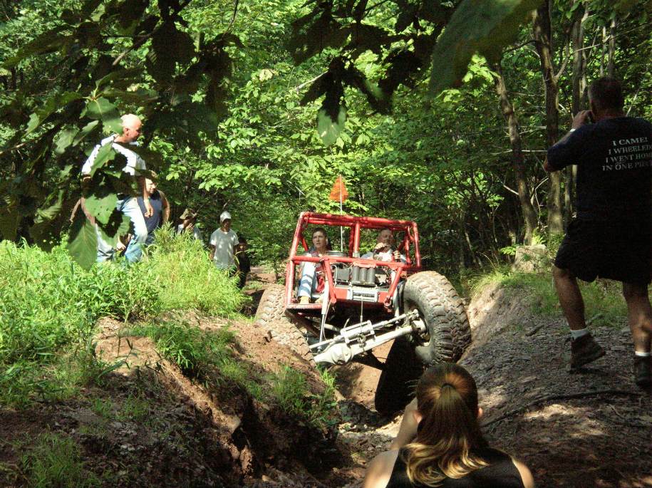 red off-road buggy climbing a muddy trail with people watching