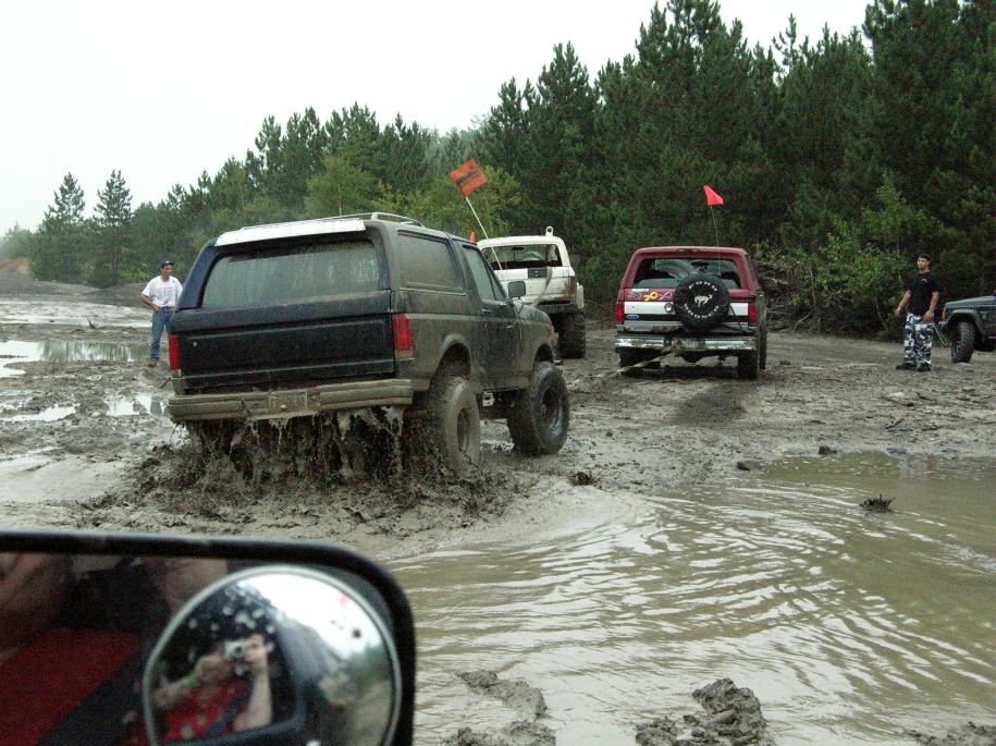 Black SUV stuck in mud, rear view. Other off-road vehicles visible