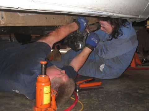 1979 Ford Bronco - Mechanics are performing maintenance on the undercarriage of a vehicle, with tools and a jack visible.