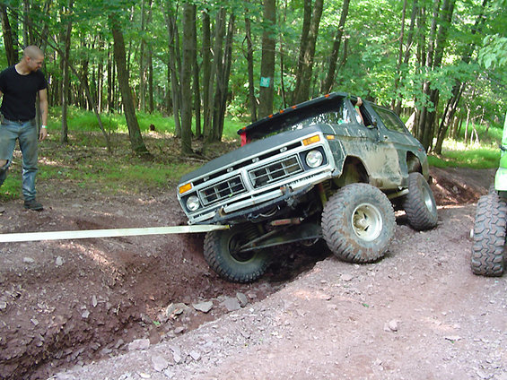 Ford Bronco stuck on dirt trail, being pulled by a strap. Man watches