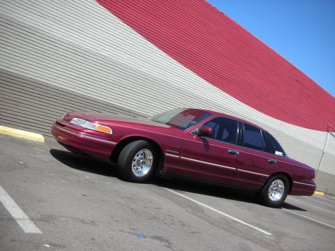 1992 Ford Crown Victoria - Maroon 1992 Ford Crown Victoria parked in a lot with a red and grey striped building in the background.