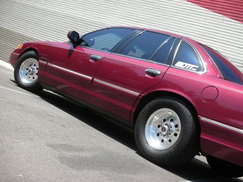 1992 Ford Crown Victoria - A maroon sedan with aftermarket wheels and tires is parked on an asphalt surface.