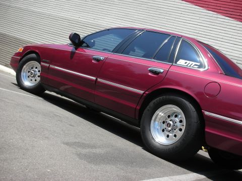 1992 Ford Crown Victoria - A maroon 1992 Ford Crown Victoria is captured from the side, its chrome trim and aftermarket drag wheels.