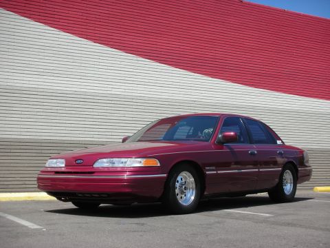 1992 Ford Crown Victoria - A maroon Ford Crown Victoria is parked in front of a building with a distinctive red and white striped facade.