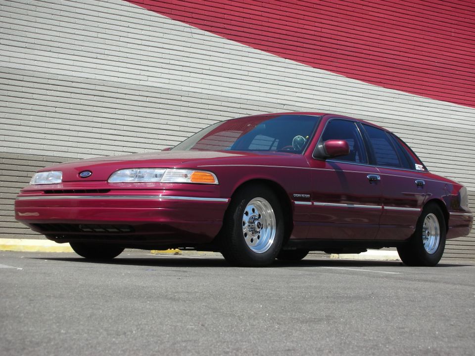 Maroon 1992 Ford Crown Victoria parked in front of a red and white striped wall, showing aftermarket wheels