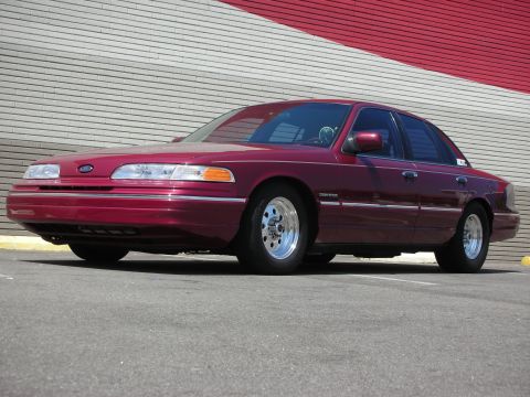 1992 Ford Crown Victoria - A maroon 1992 Ford Crown Victoria is shown from the front three-quarter view, chrome wheels and a red and white striped wall in the backgro…