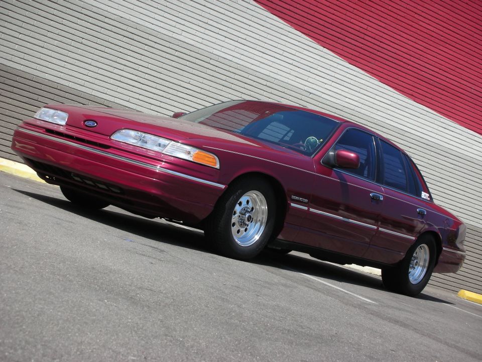 Maroon 1992 Ford Crown Victoria sedan with chrome wheels parked in front of a red and white striped wall