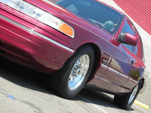 1992 Ford Crown Victoria - A close-up of a maroon 1992 Ford Crown Victoria, showing its chrome wheels and side profile.