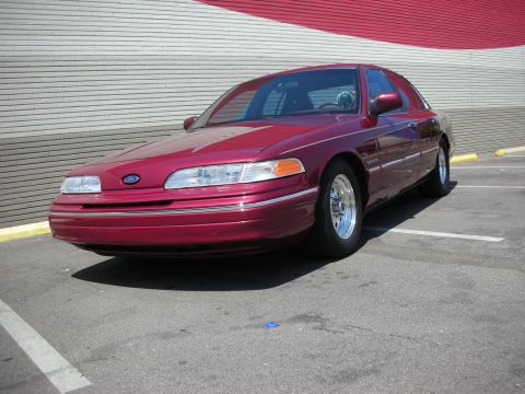 1992 Ford Crown Victoria - A red 1992 Ford Crown Victoria is parked in a lot with a red and white striped wall in the background.