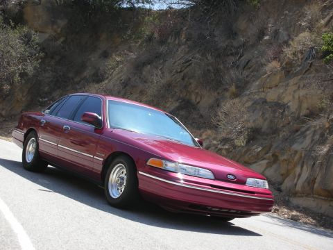 1992 Ford Crown Victoria - A maroon sedan is parked on the side of a road with a rocky hillside behind it.