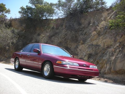 1992 Ford Crown Victoria - This maroon 1992 Ford Crown Victoria is captured from a three-quarter front view on a scenic, winding road.