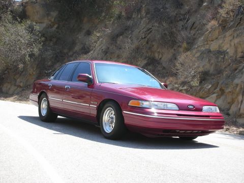1992 Ford Crown Victoria - A maroon Ford Crown Victoria is parked on the side of a road with a dry, rocky hillside in the background.