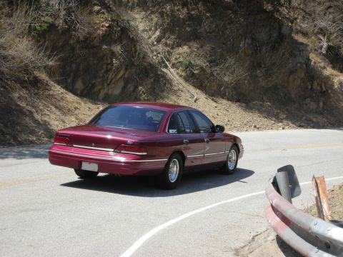 1992 Ford Crown Victoria - A maroon 1992 Ford Crown Victoria sedan navigates a curve on a sunny day.