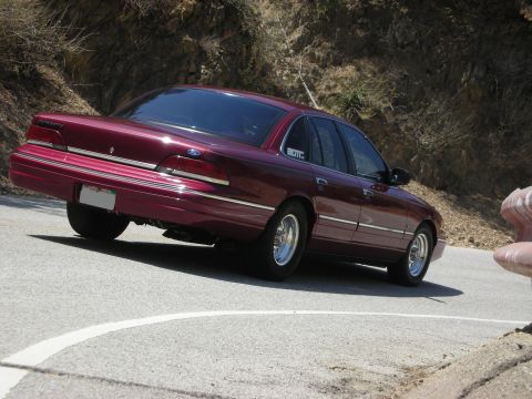 1992 Ford Crown Victoria - Maroon 1992 Ford Crown Victoria seen from the rear on a winding road.