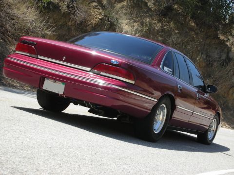 1992 Ford Crown Victoria - A maroon 1992 Ford Crown Victoria is shown from the rear on a paved road with a rocky hillside behind it.