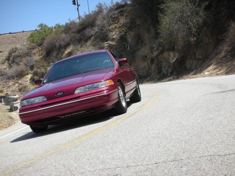 1992 Ford Crown Victoria - A maroon 1992 Ford Crown Victoria navigates a curve on a sunny day.