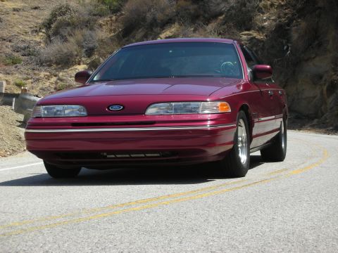 1992 Ford Crown Victoria - A maroon 1992 Ford Crown Victoria is seen from the front on a winding road with hills in the background.