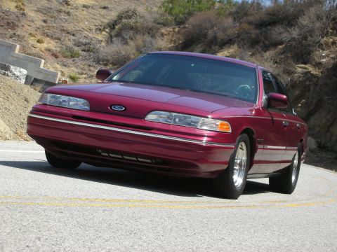 1992 Ford Crown Victoria - Maroon 1992 Ford Crown Victoria driving on a paved road with hills in the background.