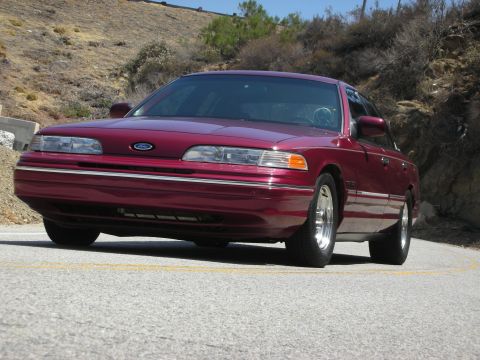 1992 Ford Crown Victoria - A maroon 1992 Ford Crown Victoria is shown from the front on a road with hills in the background.