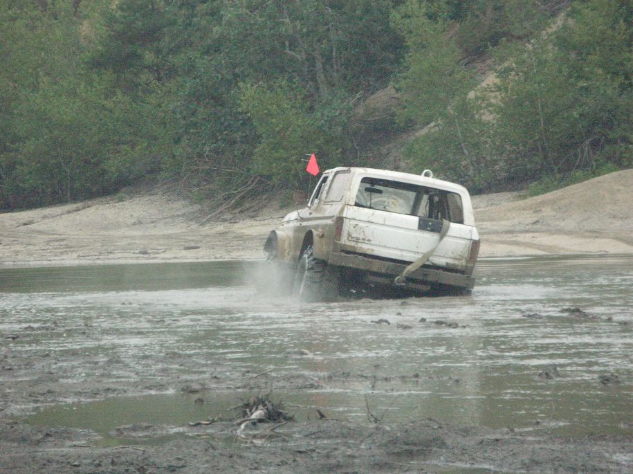 White SUV driving through mud, kicking up water. Red flag on top