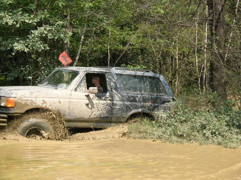 Mud-covered Ford Bronco stuck in a muddy puddle, driver visible inside