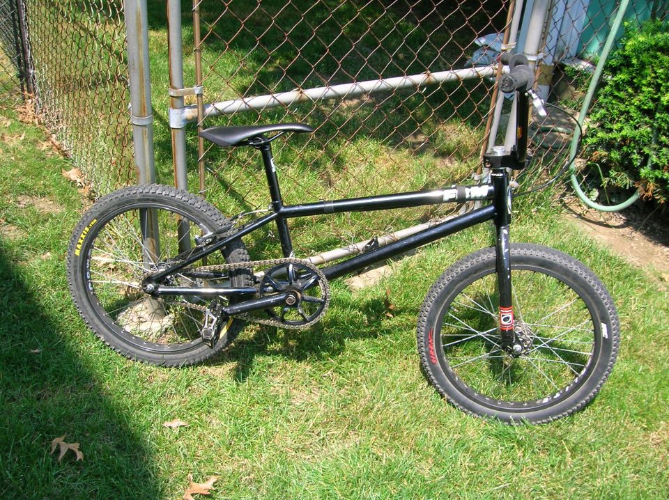 Black BMX bicycle with knobby tires parked on grass next to a chain-link fence