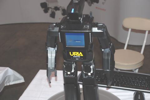 1996 Ford Bronco - A black robot with a screen and the URIA ROBOTIS logo is displayed in a room with a keyboard and a chair.