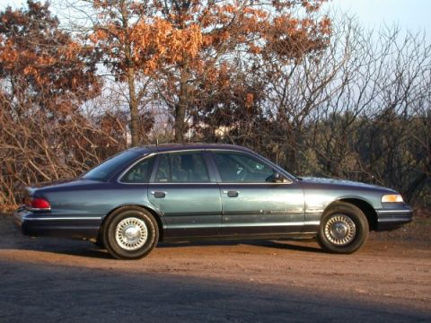 1995 Ford Crown Victoria - A 1995 Ford Crown Victoria sedan is seen from the side, parked outdoors with trees in the background.