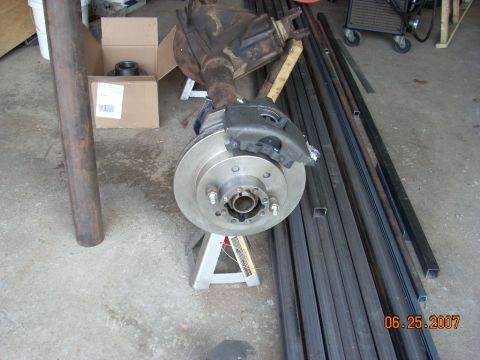 2000 Chevrolet Tahoe - Rear axle assembly with disc brake and caliper, supported by jack stands, with metal bars in the background.