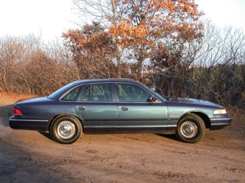 1995 Ford Crown Victoria - A 1995 Ford Crown Victoria is shown from the side, parked outdoors with dry brush and trees behind it.