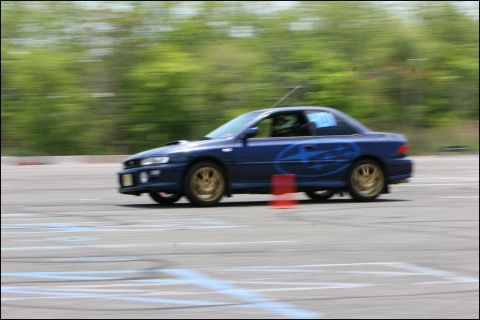 2001 Mercury Grand Marquis - Blue Subaru Impreza WRX STI navigates a race track, passing a traffic cone.