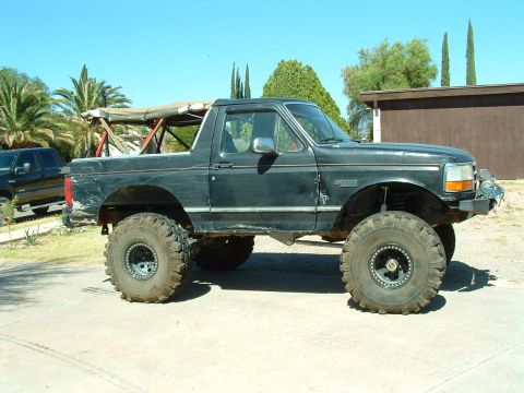 1993 Ford Bronco - A modified black Ford Bronco with large off-road tires is parked outside on a sunny day.